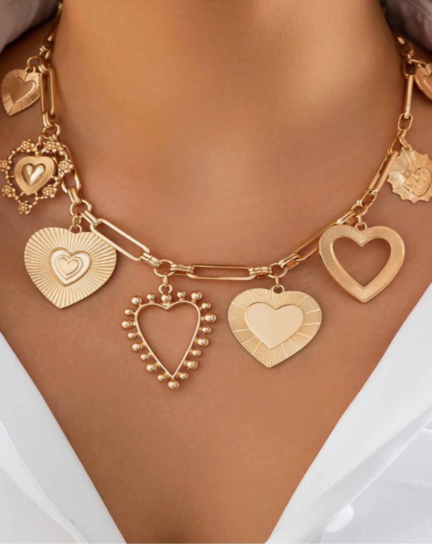Gold necklace with heart-shaped charms on a woman wearing a white top.