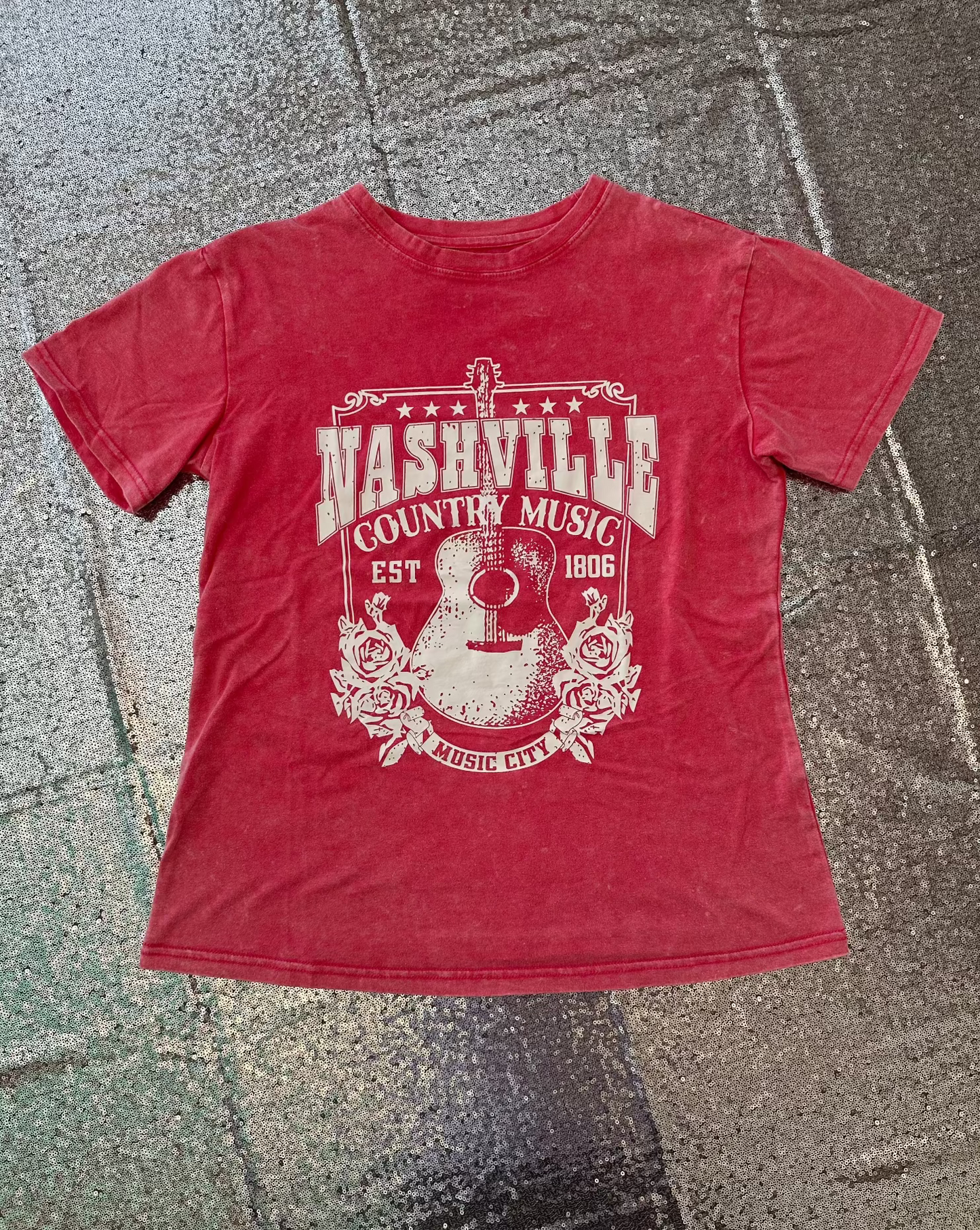 Pink t-shirt with 'Nashville Country Music' graphic on a textured surface