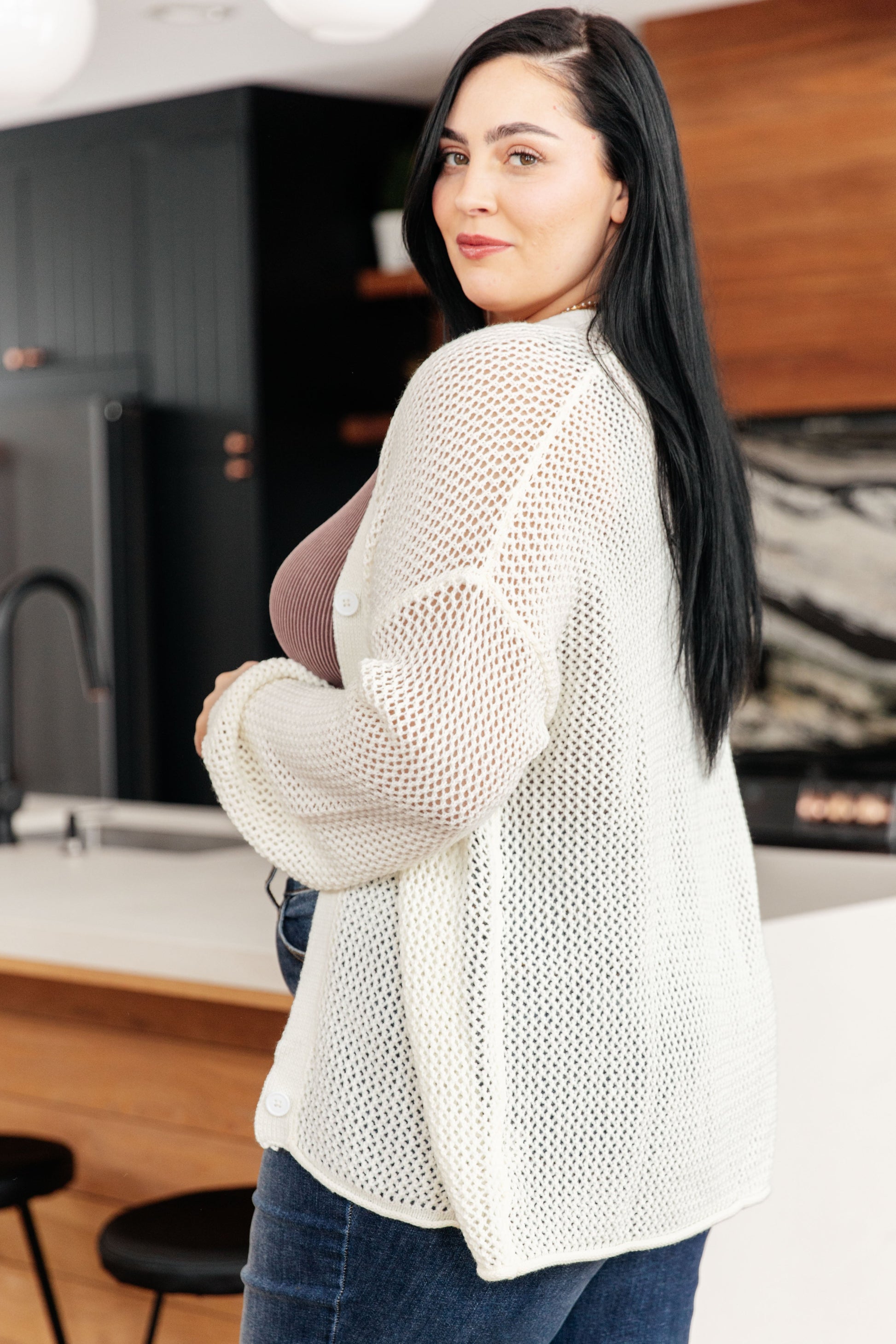 a woman wearing a white cardigan with jeans.