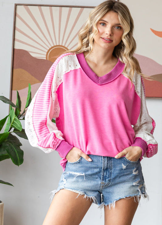 Woman wearing a pink sweater with white sleeves and denim shorts in a room with a colorful abstract painting.