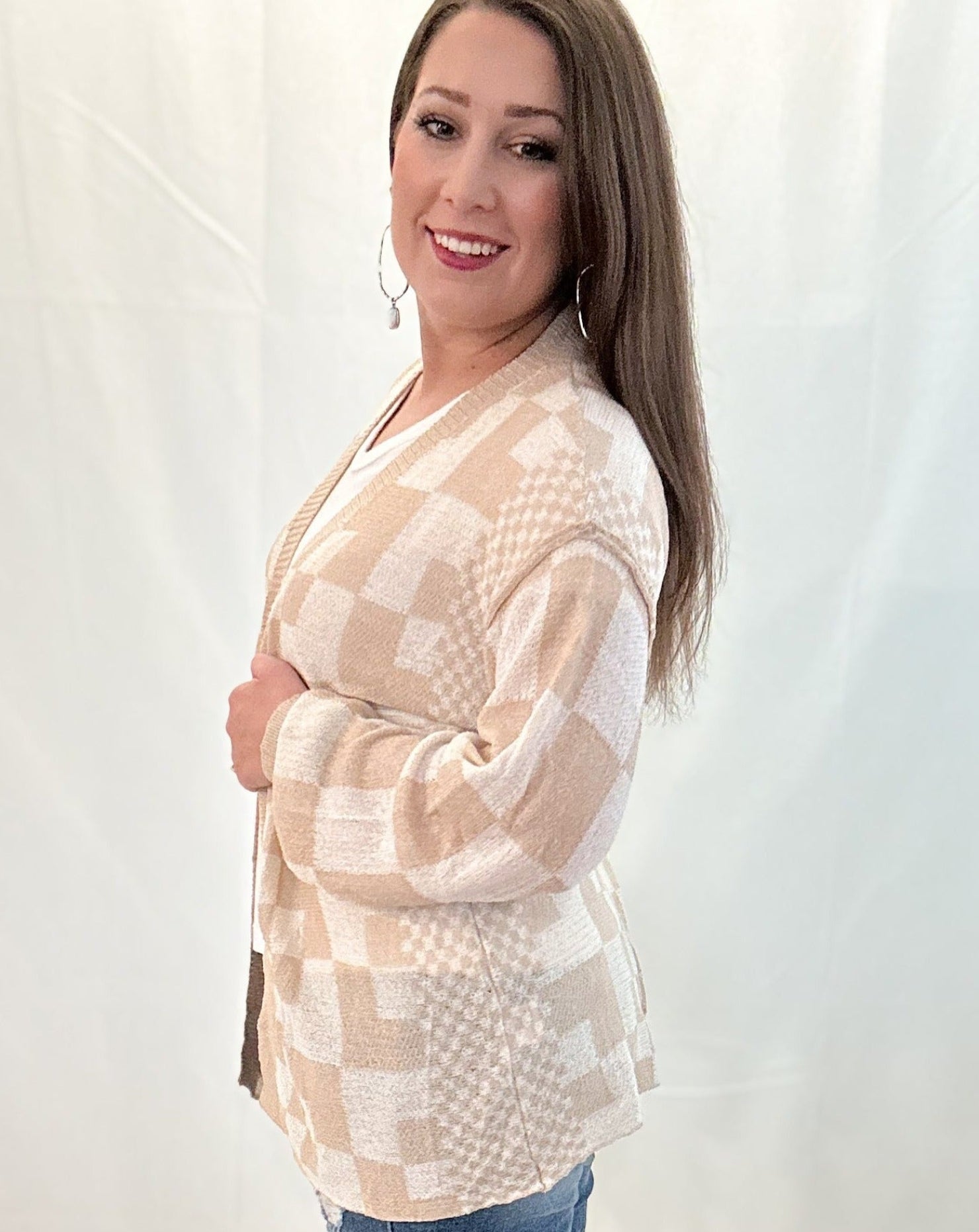 Woman wearing a beige and white checkered cardigan against a plain background