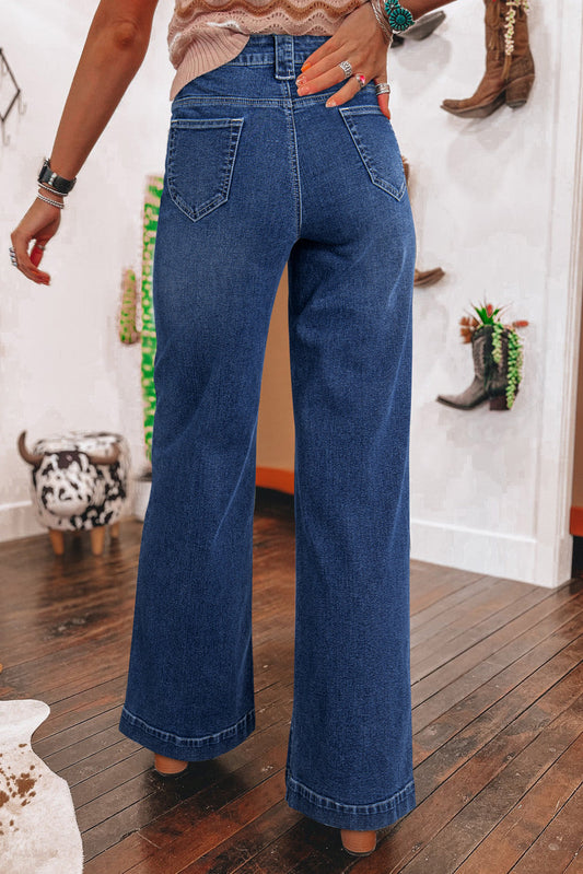Women wearing blue jeans in a room with wooden floor and white walls.